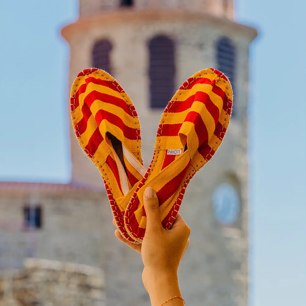 Espadrille rayée rouge et jaune portée à la main